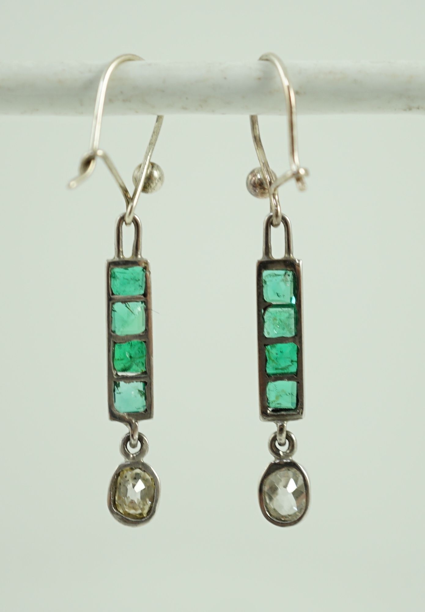 A pair of white gold, four stone emerald and single stone oval cut diamond set drop earrings